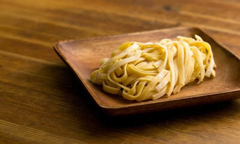 צלחת עץ עם אטריות מעלה מונחת על שולחן עץ