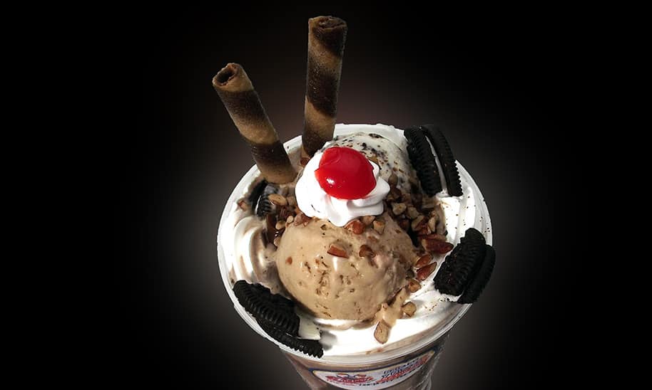 צילום מלמעלה של כוס עם גלידה עוגיות אוראו ודובדבן על קצפת
