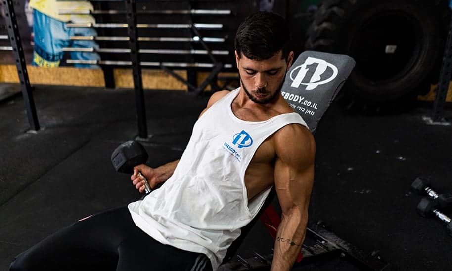 גבר צעיר עם גופייה לבנה מרים משקולות על ספת כושר