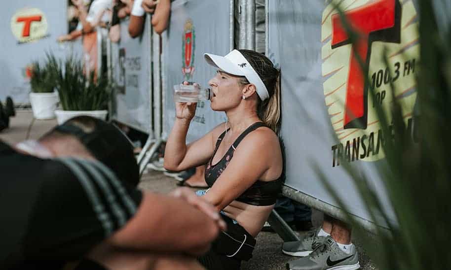 אישה יושבת בצד נשענת על הקיר שותה מים בעייפות