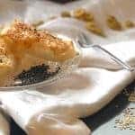 בורקס עשוי מדפי אורז על מפה לבנה ולידו חתיכות של זיתים, סומסום מפוזר ומזלג