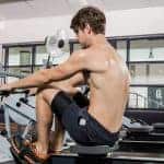 גבר יושב במכונת חתירה בלי חולצה אוחז בידיות המתקן