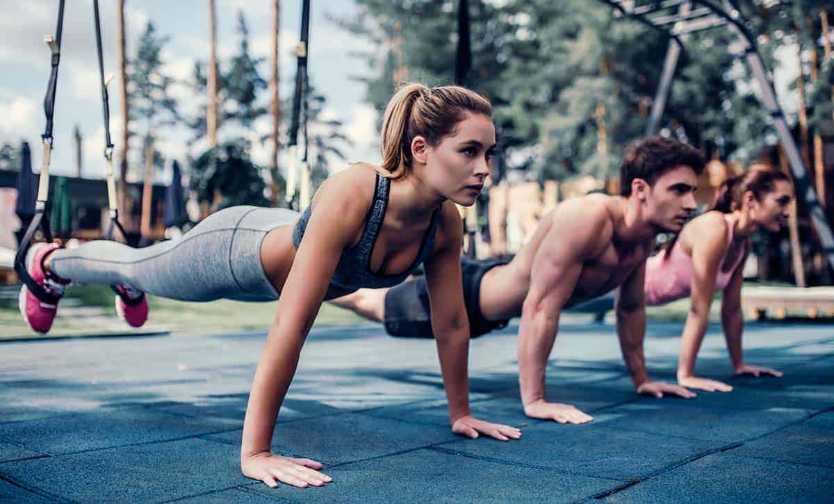 2 נשים וגבר במנח של שכיבת סמיכה עם רגליים באוויר בTRX