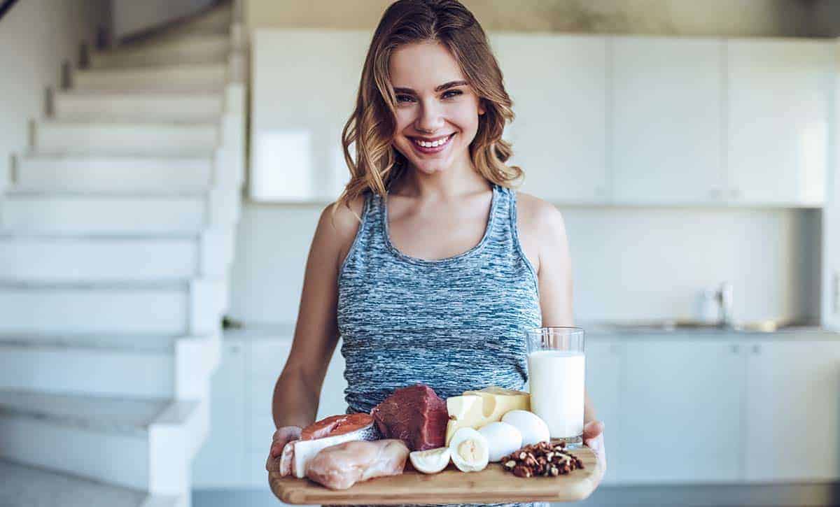 אישה מחייכת מחזיקה פלטה מעץ עם בשר, גבינות וסלמון