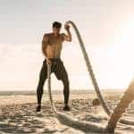 גבר מבצע אימון טבטה עם חבלים על חוף הים באמצע היום