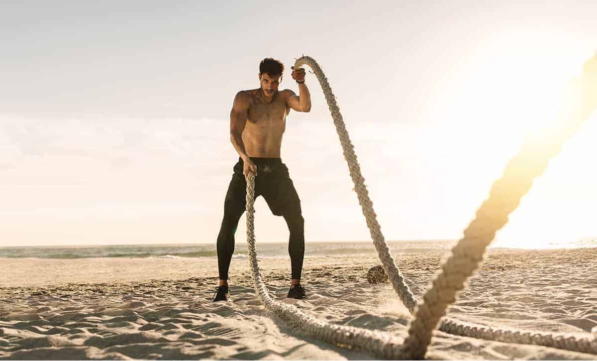 גבר מבצע אימון טבטה עם חבלים על חוף הים באמצע היום