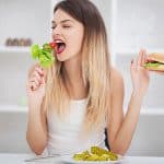 אישה אוכלת סלט עם יד אחת ודוחפת יד שמציעה לה המבורגר עם יד ימין