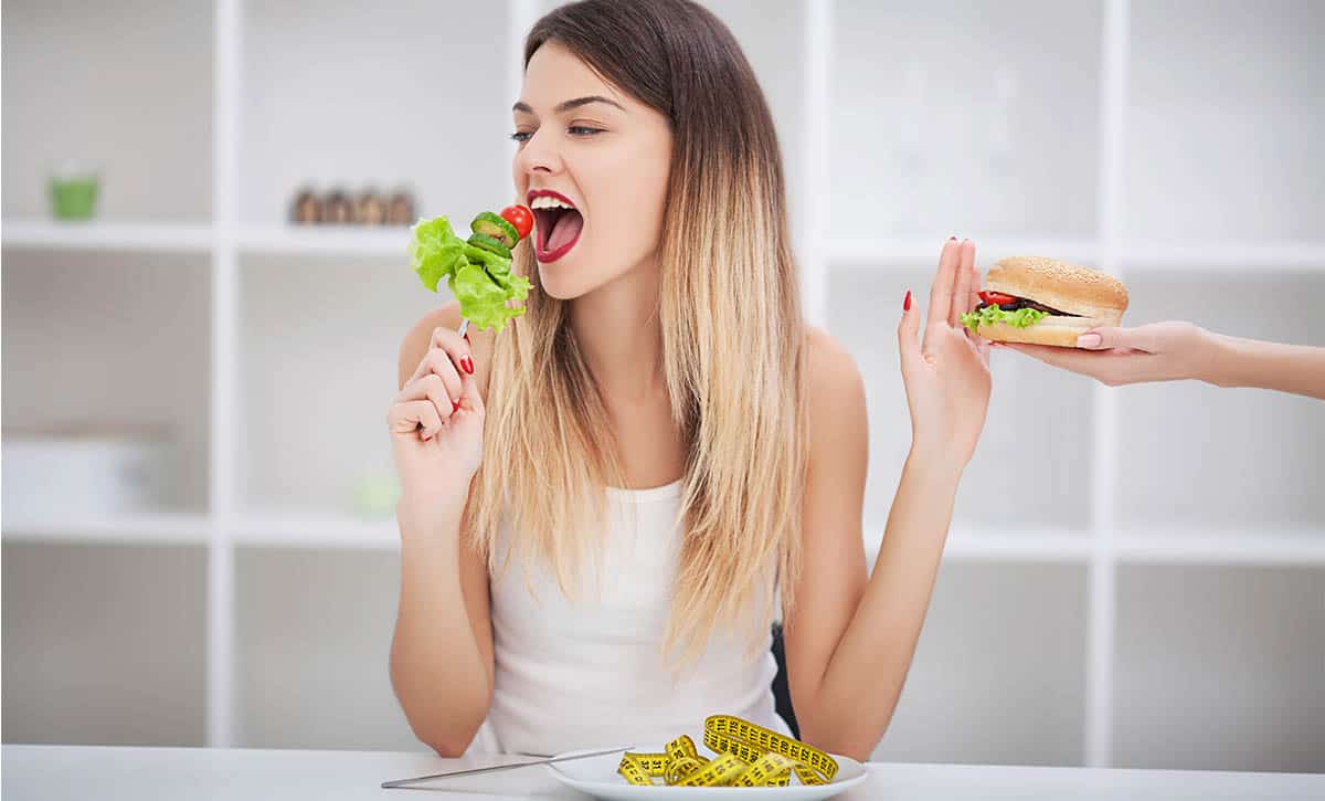 אישה אוכלת סלט עם יד אחת ודוחפת יד שמציעה לה המבורגר עם יד ימין
