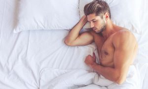 גבר שרירי ישן על מיטה לבנה